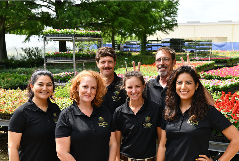 Newton Nurseries' Employees Smiling In Front Of Flowers Newton Nurseries' Employees Smiling In Front Of Flowers