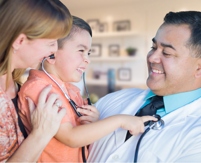 A Doctor Holding A Child Wearing A Stethoscope And Smiling Next To His Mom